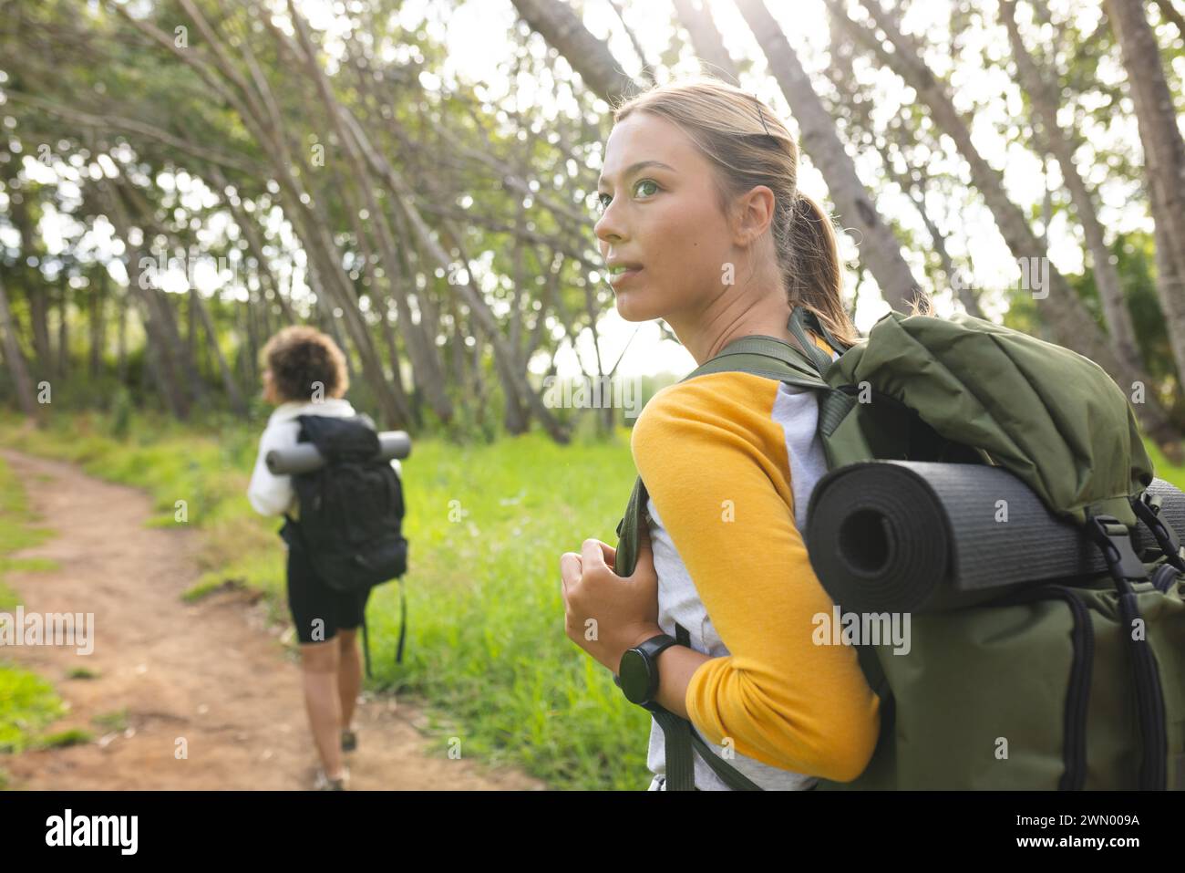 Two women, equipped for hiking, explore a tranquil forest trail together. Stock Photo