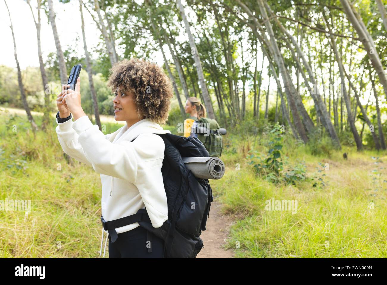 Two women, one biracial and one Caucasian, explore nature, taking selfies on a hike. Stock Photo