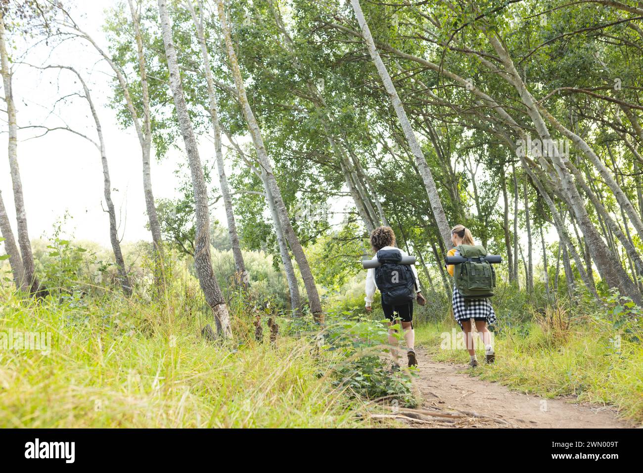Two women are hiking through a forested trail during the daytime with ...
