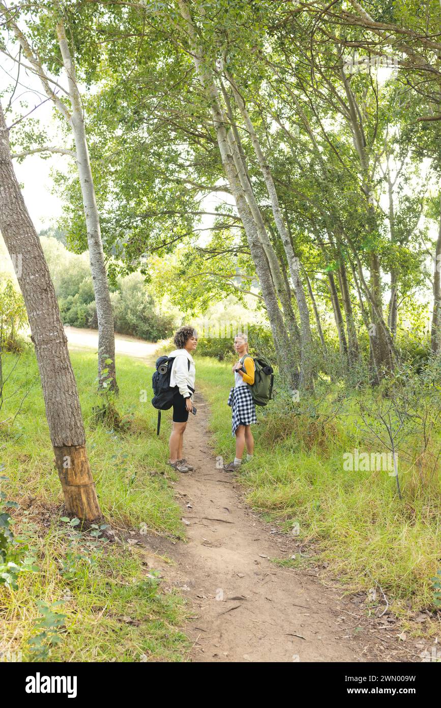 Two women pause for a chat on a hike on a dirt path surrounded by greenery, with copy space Stock Photo