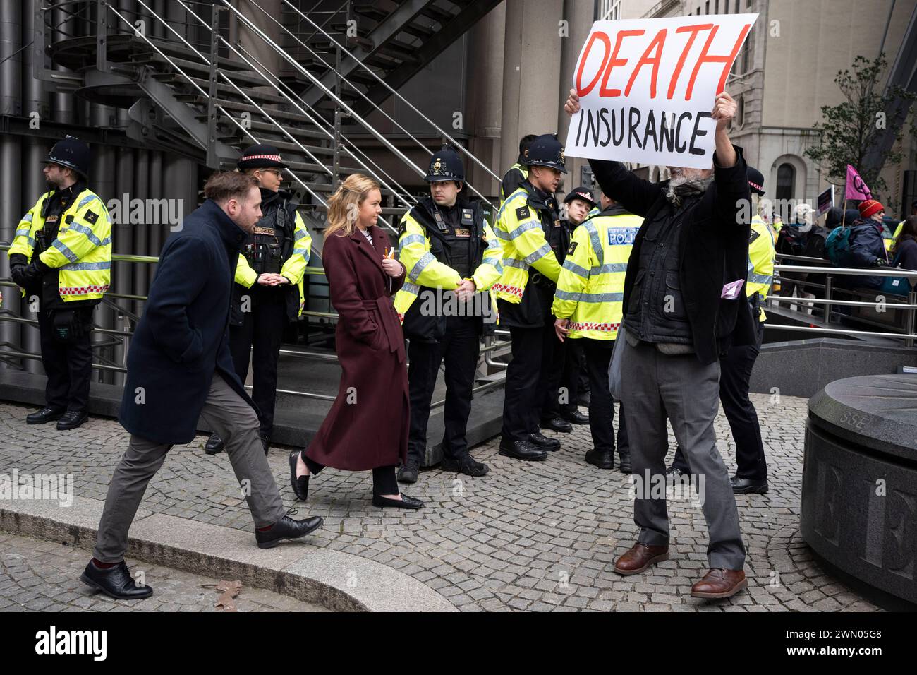 City workers pass through climate change protesters with Extinction Rebellion who are protesting outside city underwriting institution, Lloyds of London in the City of London, the capital's financial district, on 28th February 2024, in London, England. Stock Photo
