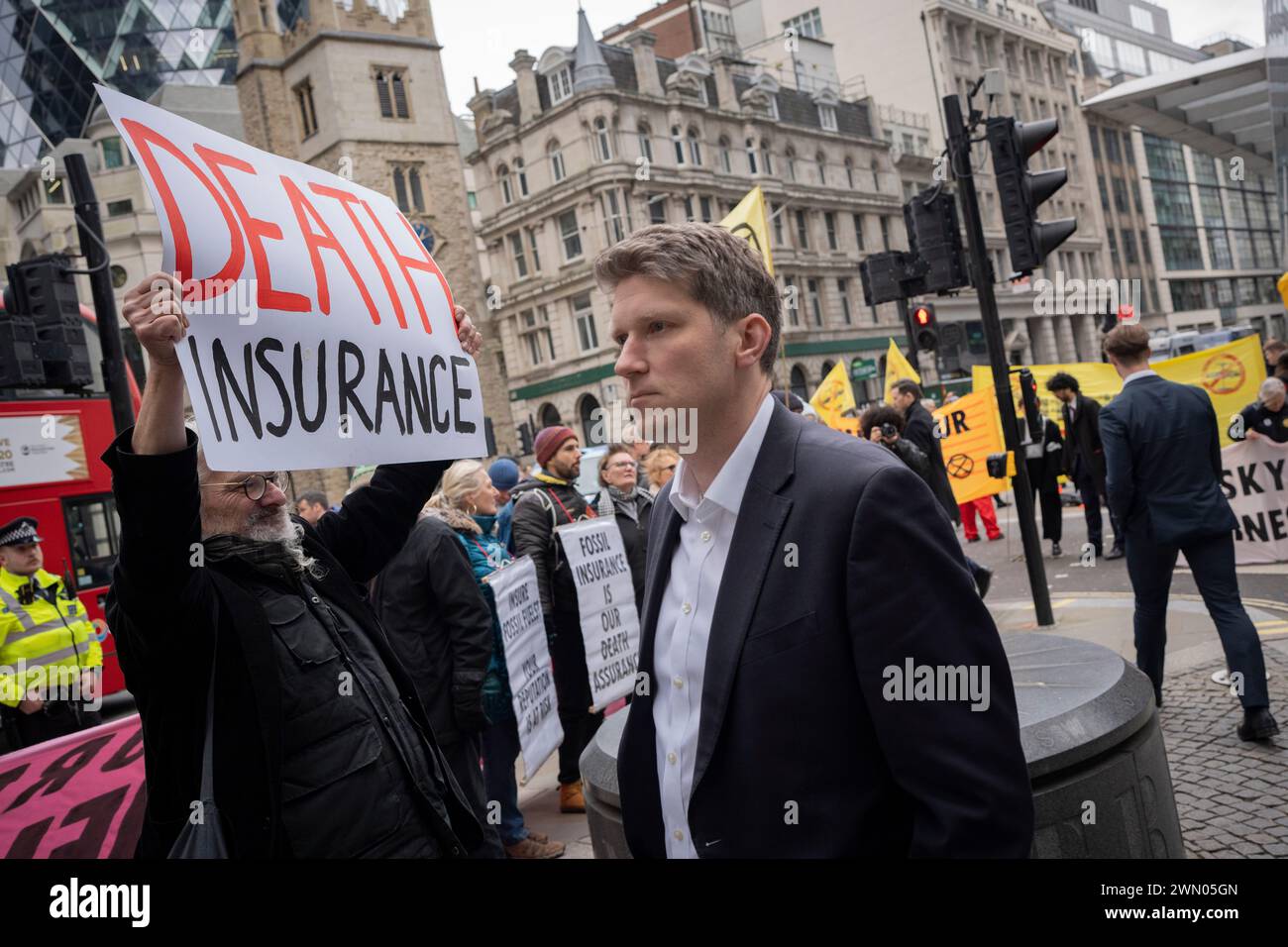 City workers pass through climate change campaigners with Extinction Rebellion who are protesting outside city underwriting institution, Lloyds of London in the City of London, the capital's financial district, on 28th February 2024, in London, England. Stock Photo