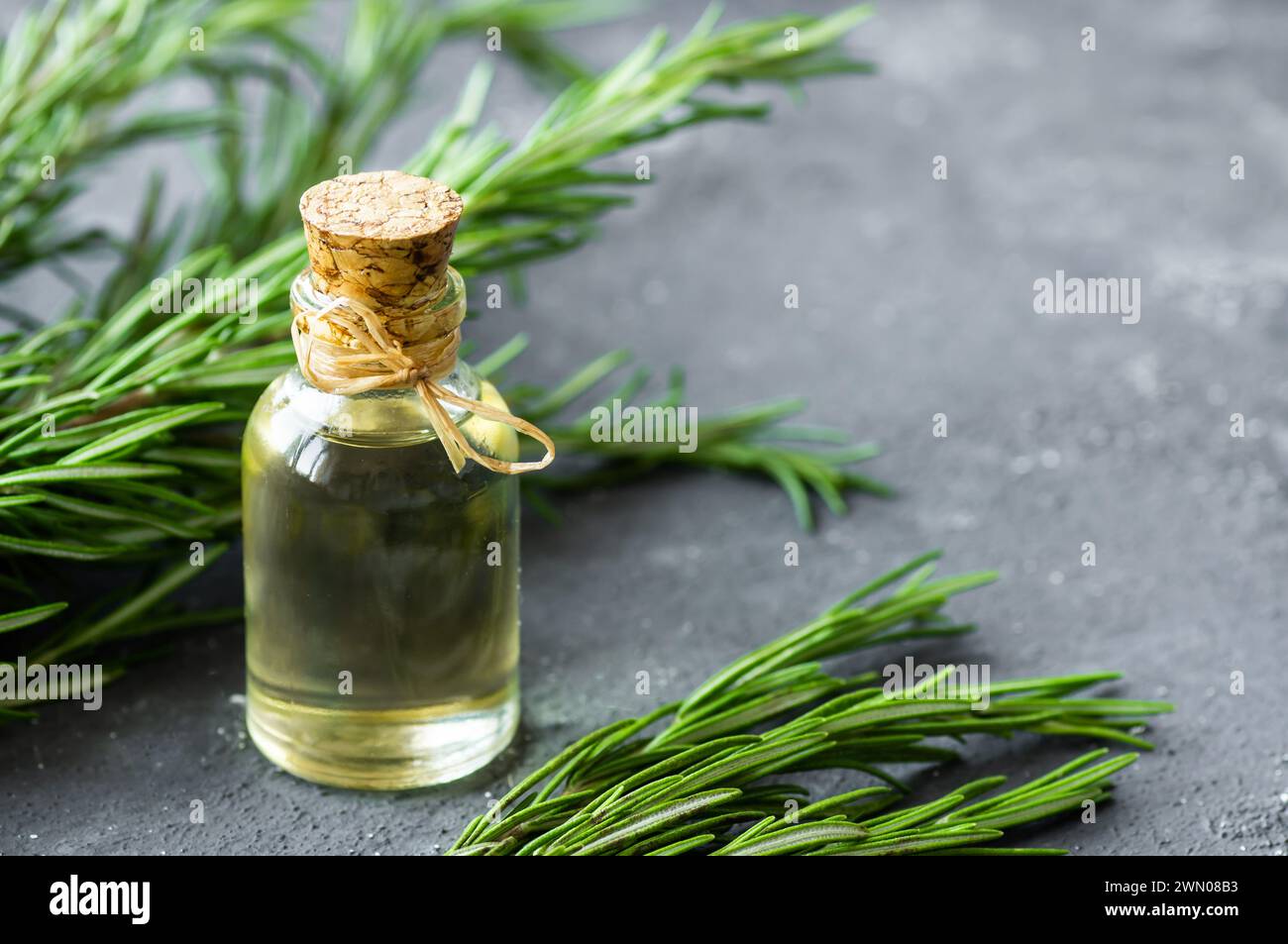 Glass bottle of essential rosemary oil with rosemary branch on rustic background. herbal oil concept, Rosmarinus Officinalis Stock Photo