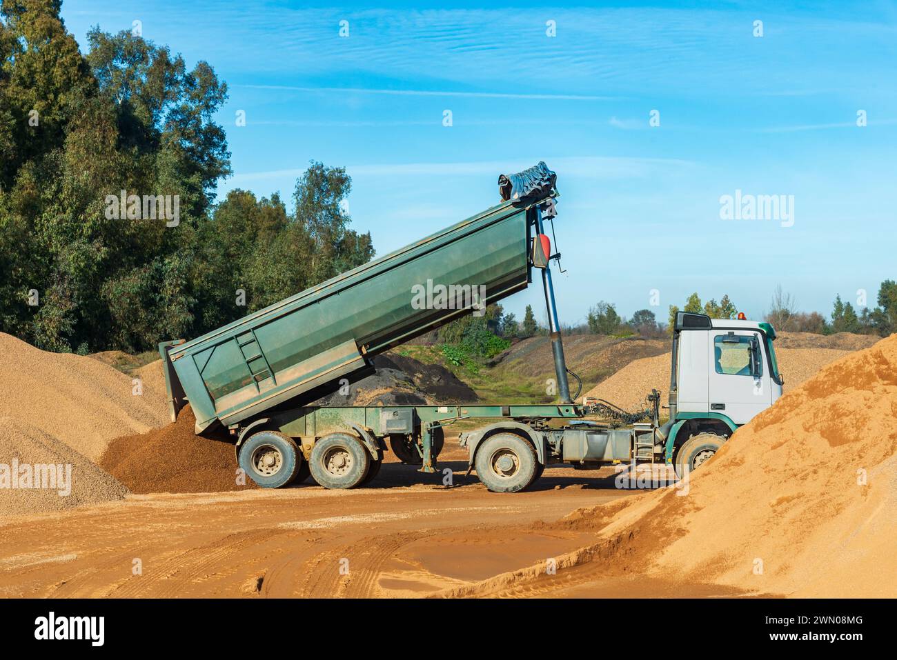 Tilting truck for transporting aggregates with the raised box unloading sand in a quarry. Stock Photo