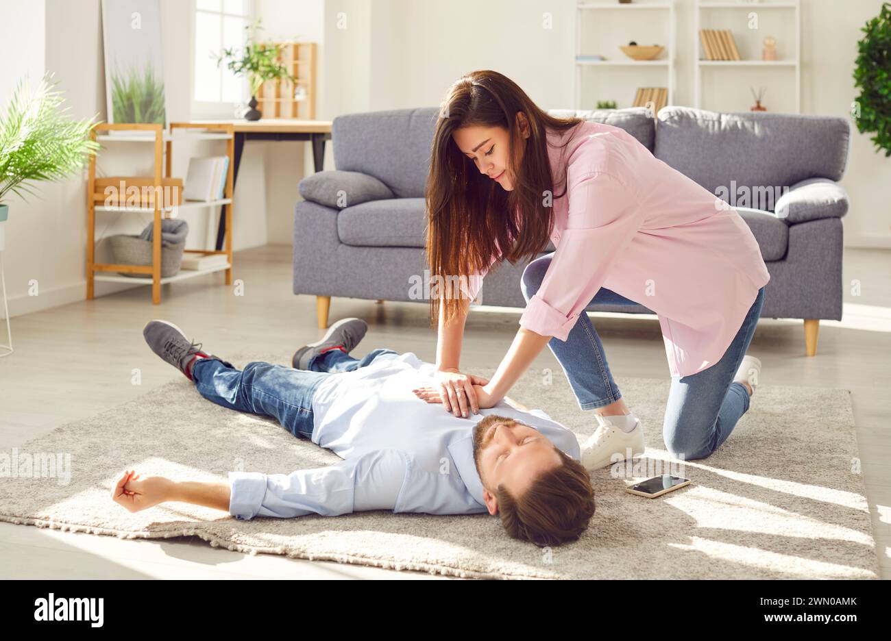 Young woman doing CPR on unconscious man lying on the floor at home. Stock Photo