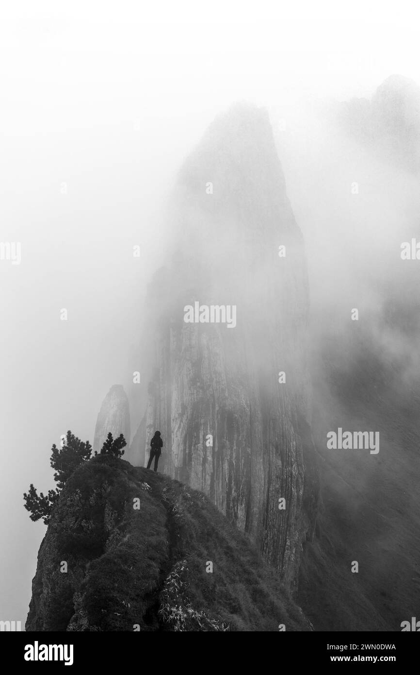 A hiker standing in front of the famous Swiss Alps peak Saxer Lucke with stunning rock formation in rising mist and fog Stock Photo
