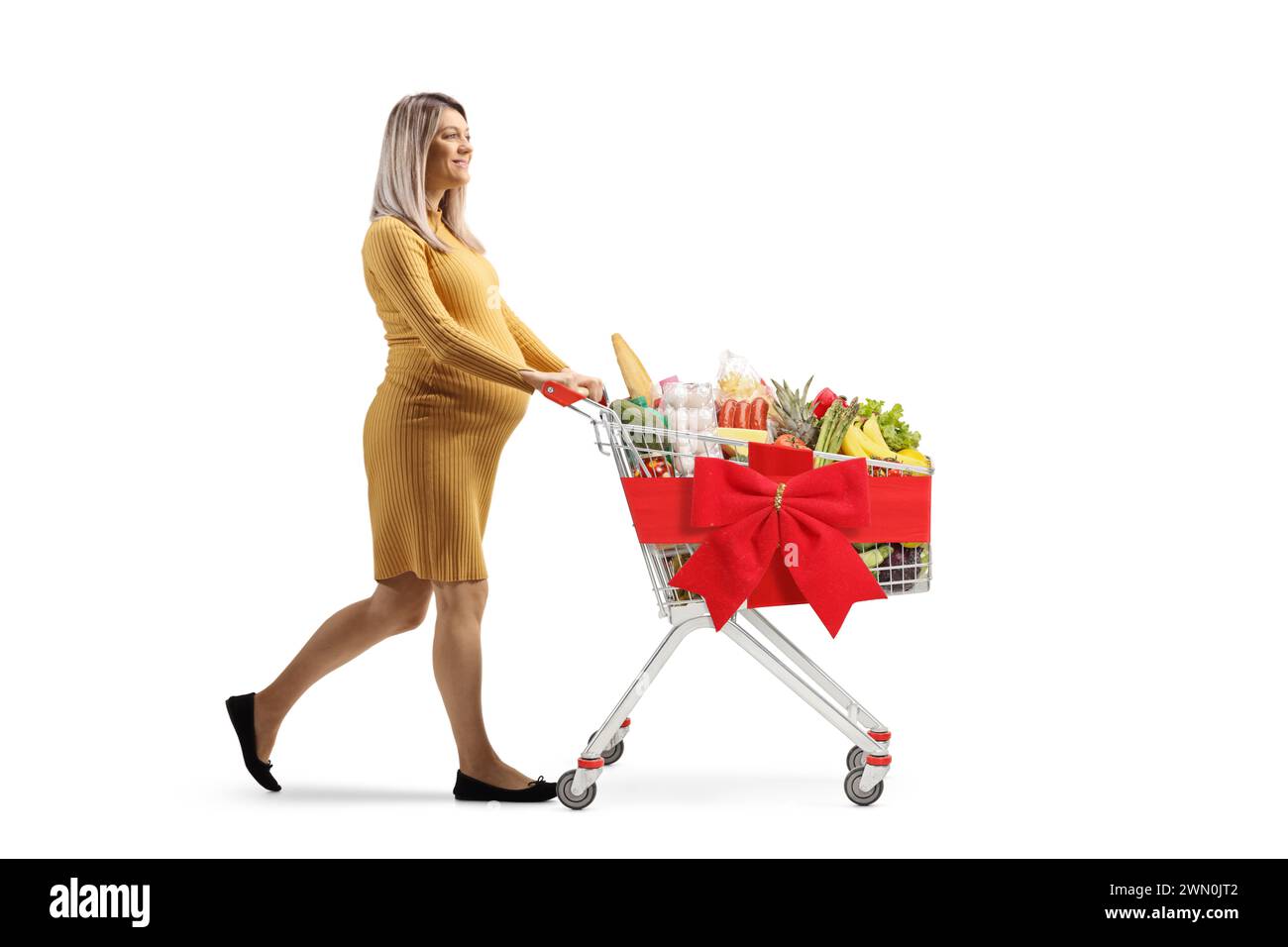 Full length profile shot of a pregnant woman pushing a shopping cart with red ribbon bow isolated on white background Stock Photo