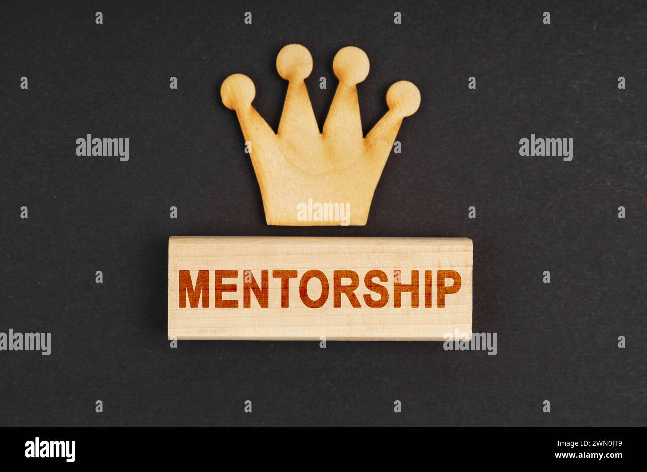 Leader concept. On a black surface there is a wooden crown and a block with the inscription - Mentorship Stock Photo