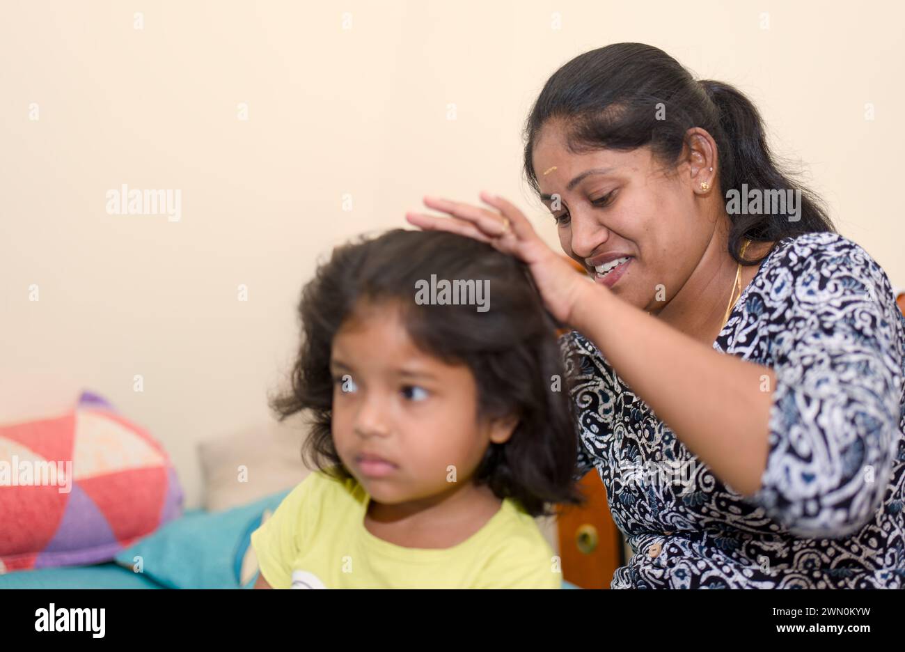 A warm image of a mother gently combing her daughter's hair in their sunlit bedroom Stock Photo
