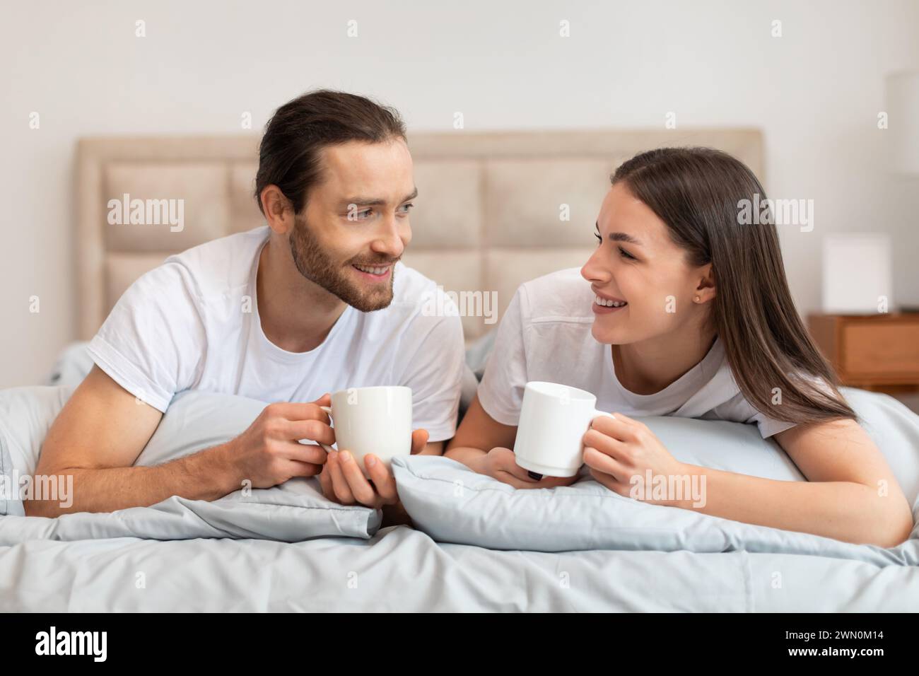 Couple enjoying coffee in bed, sharing smile and talking Stock Photo