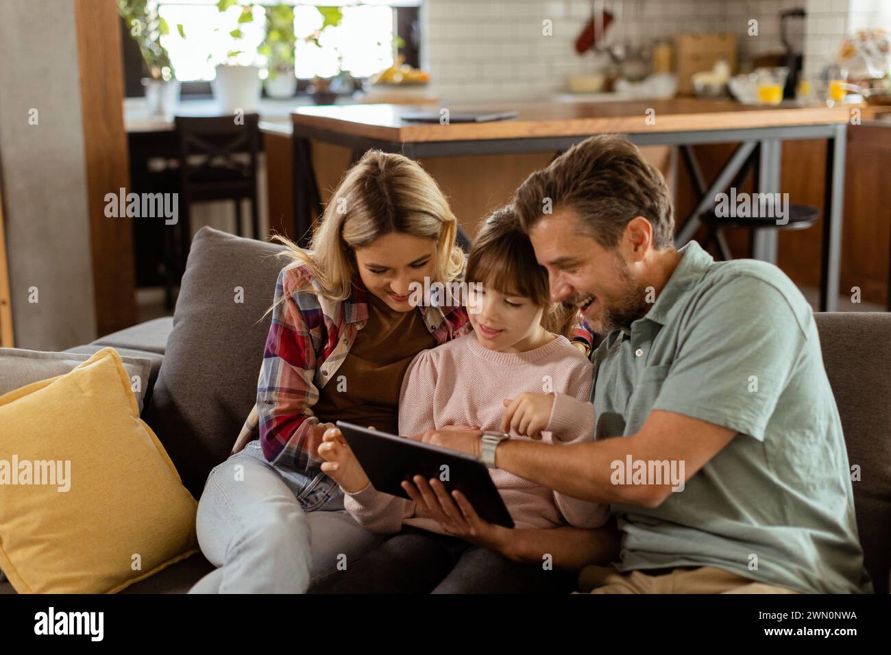 Joyful family shares a moment around a digital tablet, with smiles and togetherness in a warm home setting Stock Photo