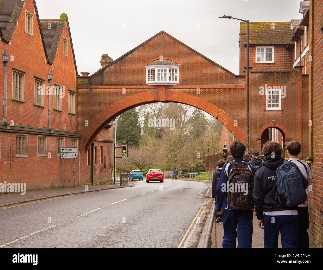 Marlborough college buildings private boarding and day school with archway across the road and pupils walking along the pavement Wiltshire UK Stock Photo