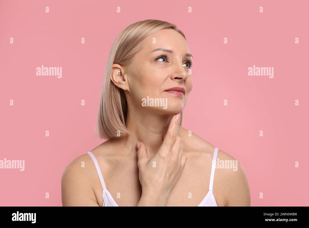Beautiful woman touching her neck on pink background Stock Photo - Alamy