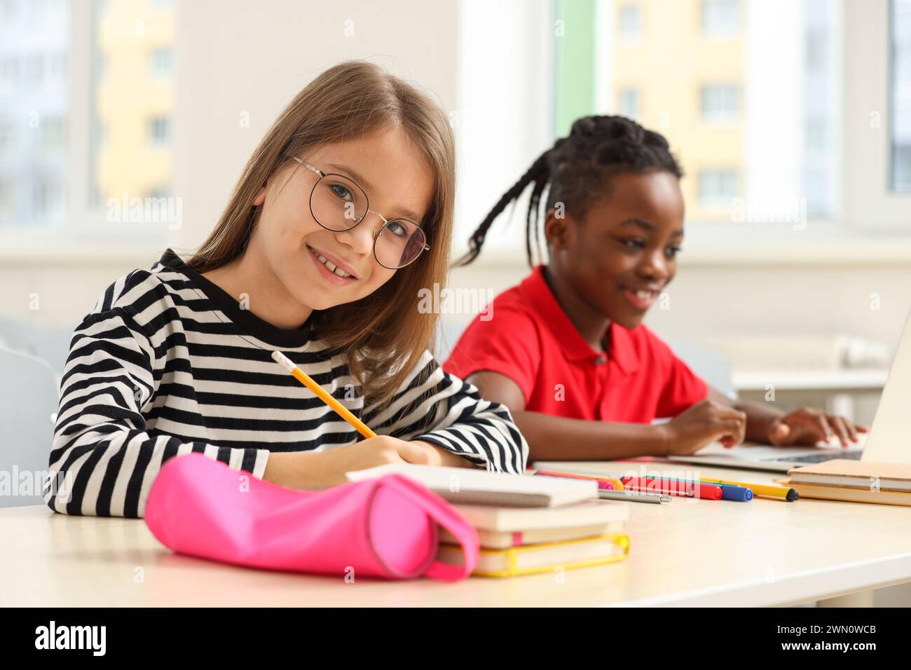 Smiling girl with her classmate studying in classroom at school Stock Photo