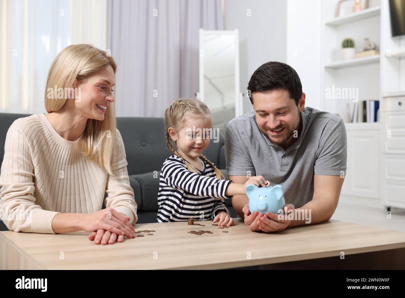 Family budget. Little girl putting coin into piggy bank while her ...