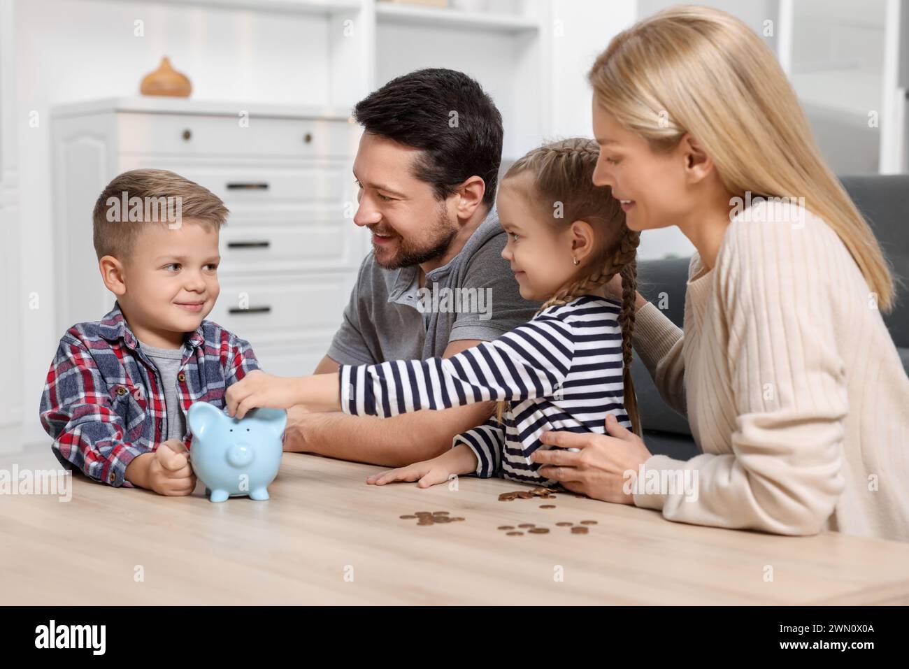 Family budget. Little boy putting coin into piggy bank while his ...