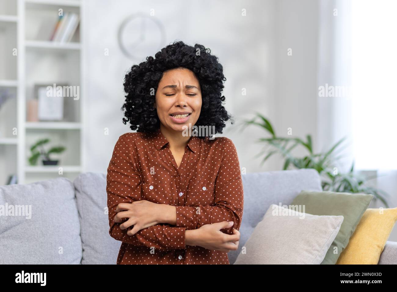 African American young woman sitting on the couch at home and shaking from the cold, having a