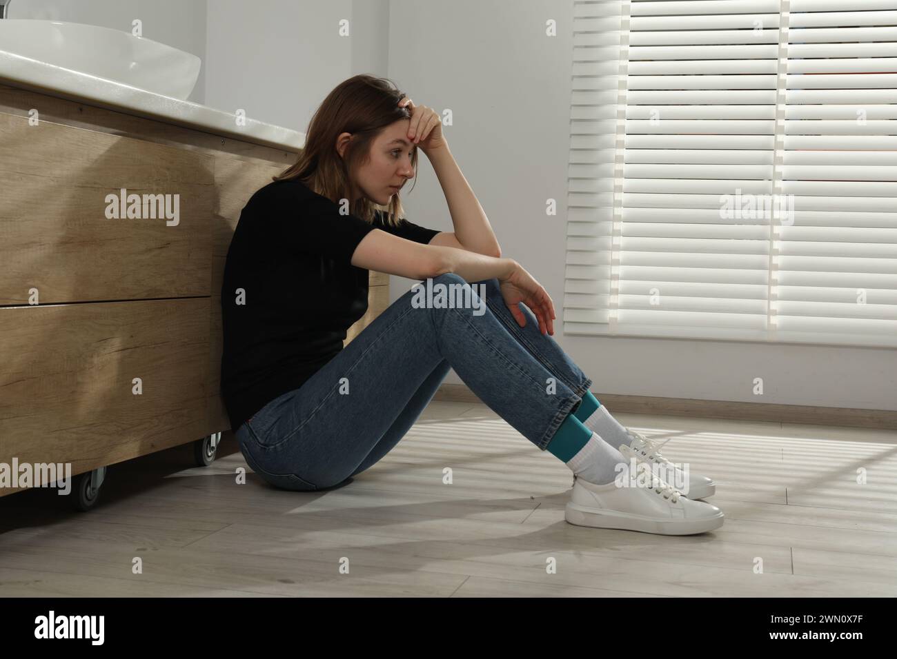 Sad young woman sitting on floor indoors Stock Photo - Alamy