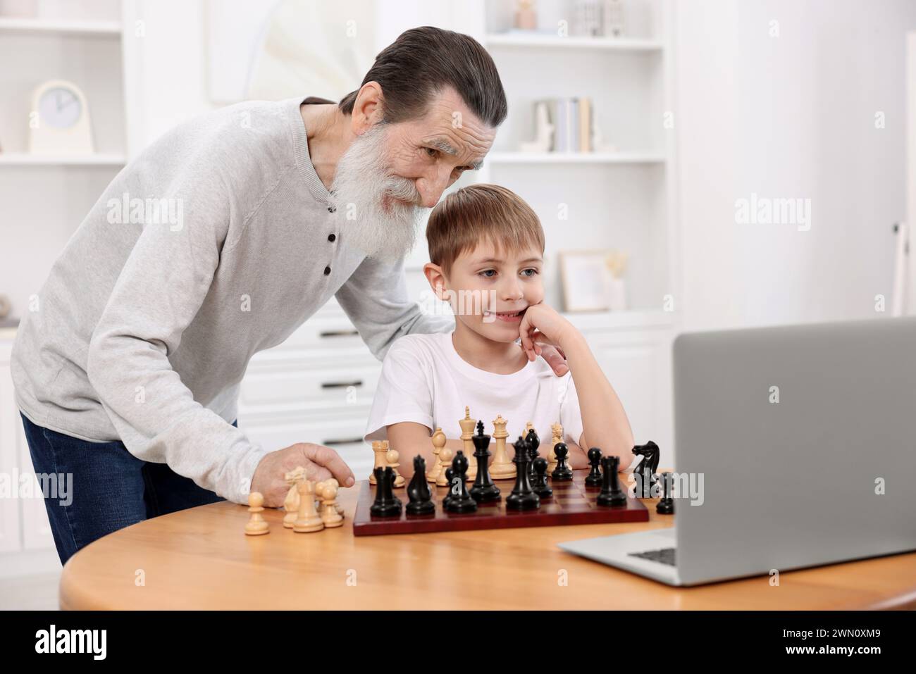 Grandfather teaching his grandson to play chess following online lesson ...