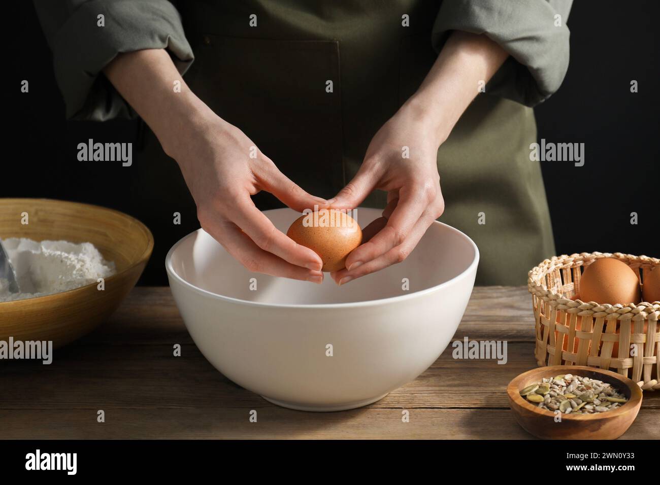 Making bread. Woman adding egg into dough at wooden table on dark