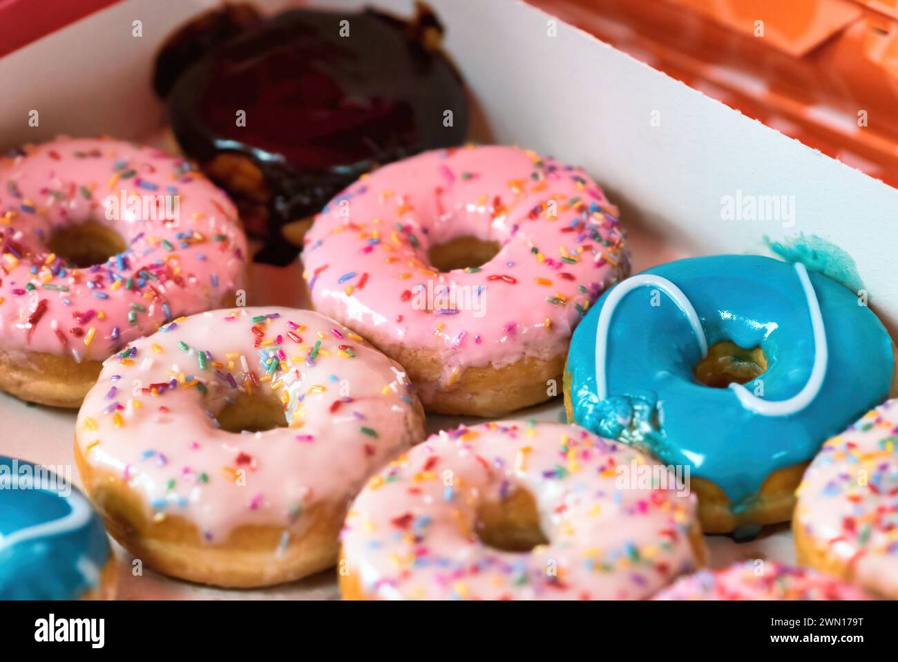 Close-up of a cardboard box full of colorful doughnuts topped with sprinkles and icing sugar coating Stock Photo