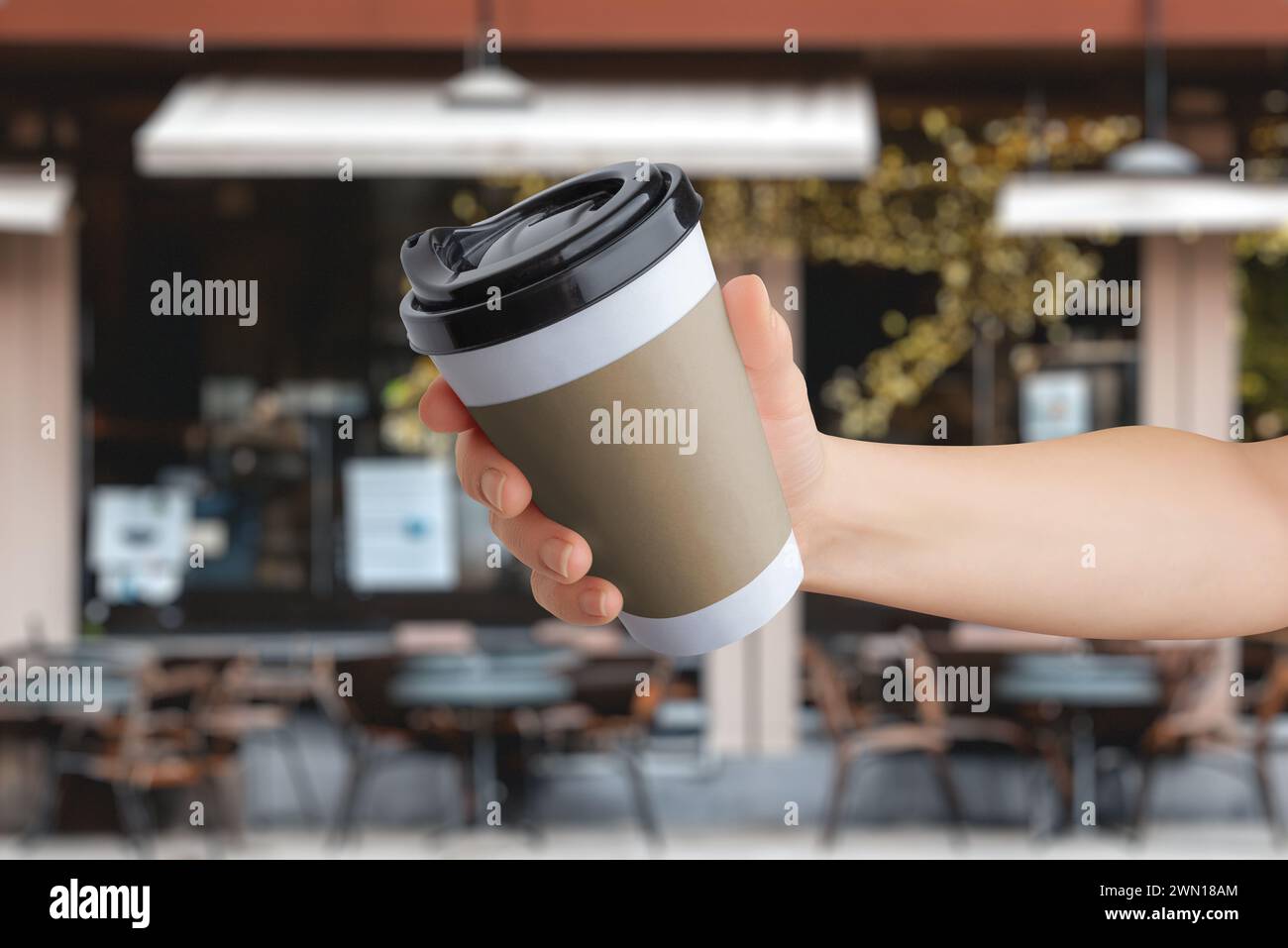 Logo mockup on a paper takeaway cup held in hand in front of a coffee shop Stock Photo