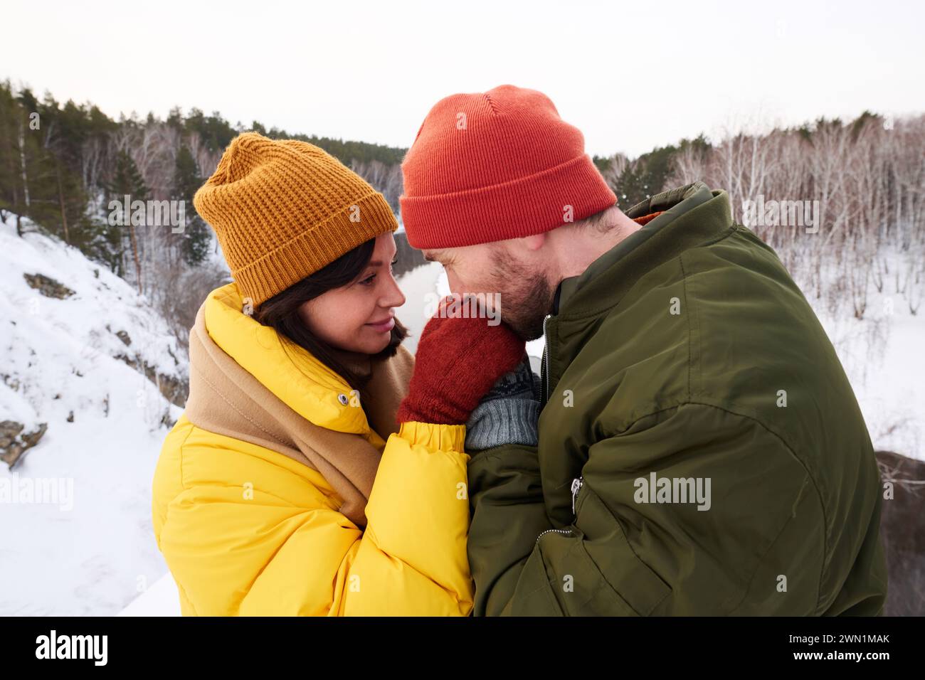 Side view shot of Caucasian couple having date in mountains on winter day, man kissing his girlfriends hand Stock Photo