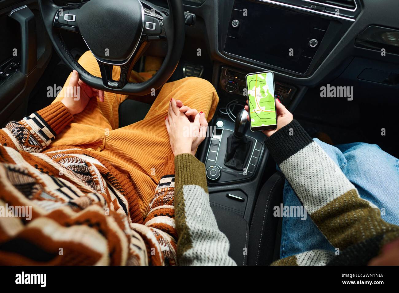 High angle view of unrecognizable tourists sitting in car holding hands and using map app on smartphone Stock Photo
