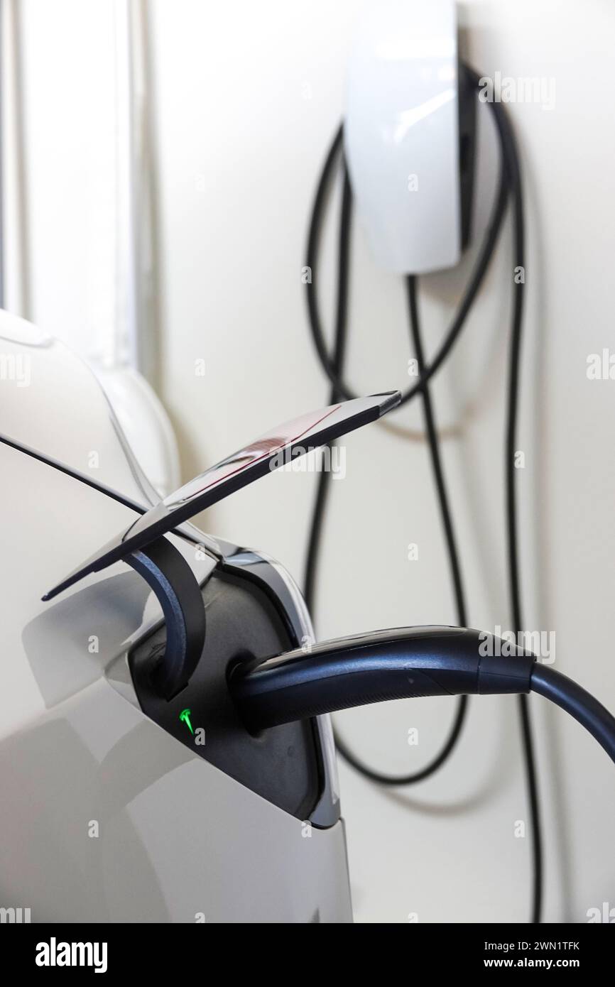 Tesla EV charging in a home garage plugged into a wall charger Stock Photo