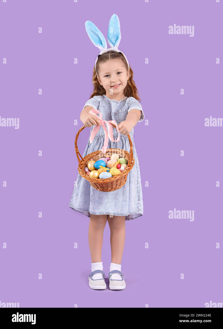 Cute little girl in bunny ears holding wicker basket with Easter eggs ...