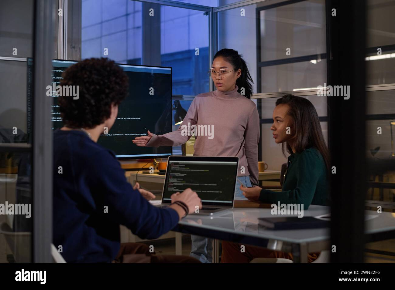 Ethnically diverse programmers working together on code at workplace in IT company office late in evening Stock Photo