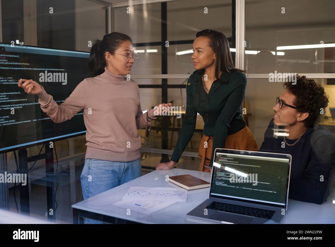 Group of three young ethnically diverse programmers working together on code in office late in evening Stock Photo