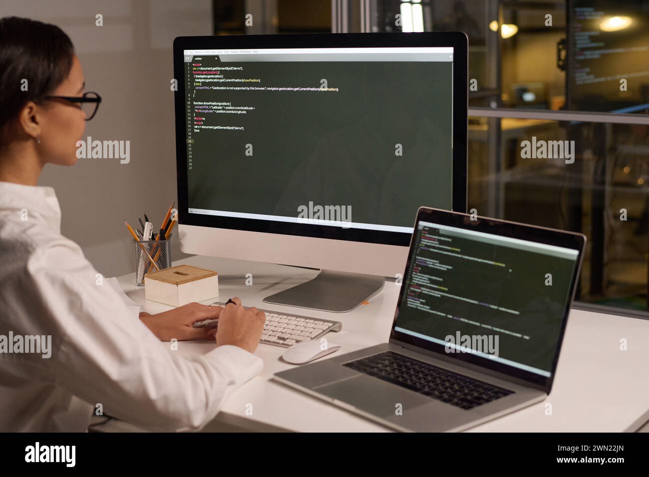 Modern young female programmer developing code typing on computer in modern office late in evening Stock Photo