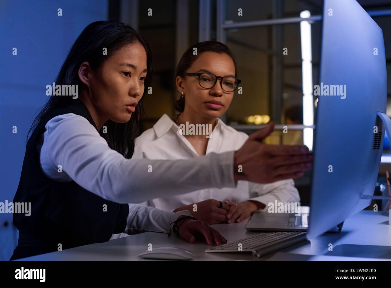 Ethnically diverse programmers working together on code at workplace in IT company office late in evening Stock Photo