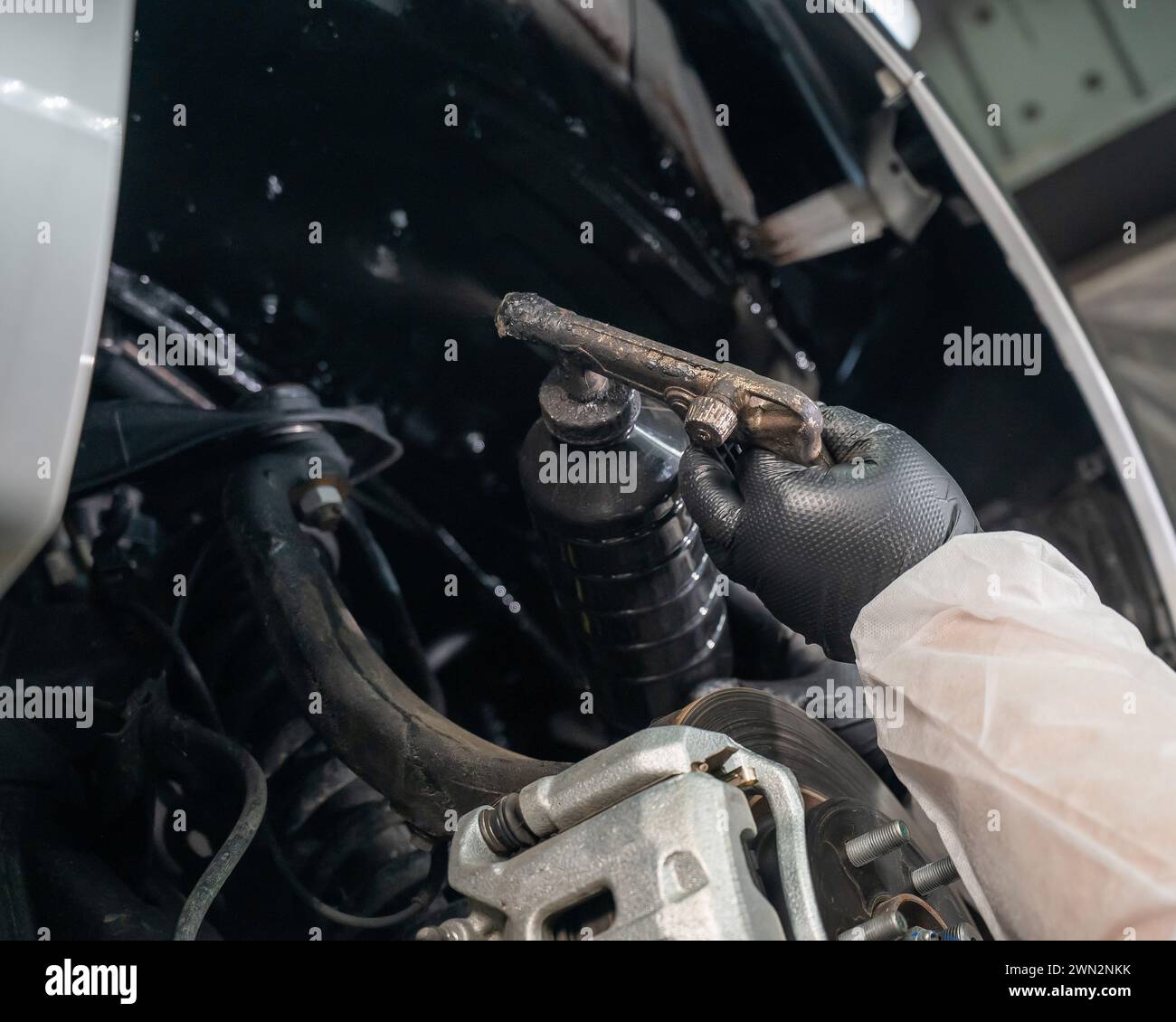 An auto mechanic applies anti-corrosion mastic to the underbody of a ...