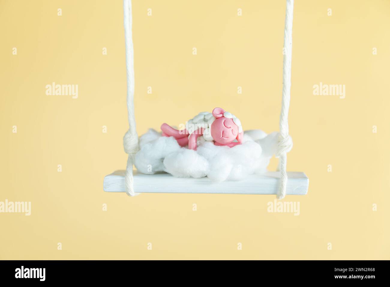 Cute plasticine sheep sleeps on a swing. Good night sweet dreams. Yellow background, copy space. Stock Photo
