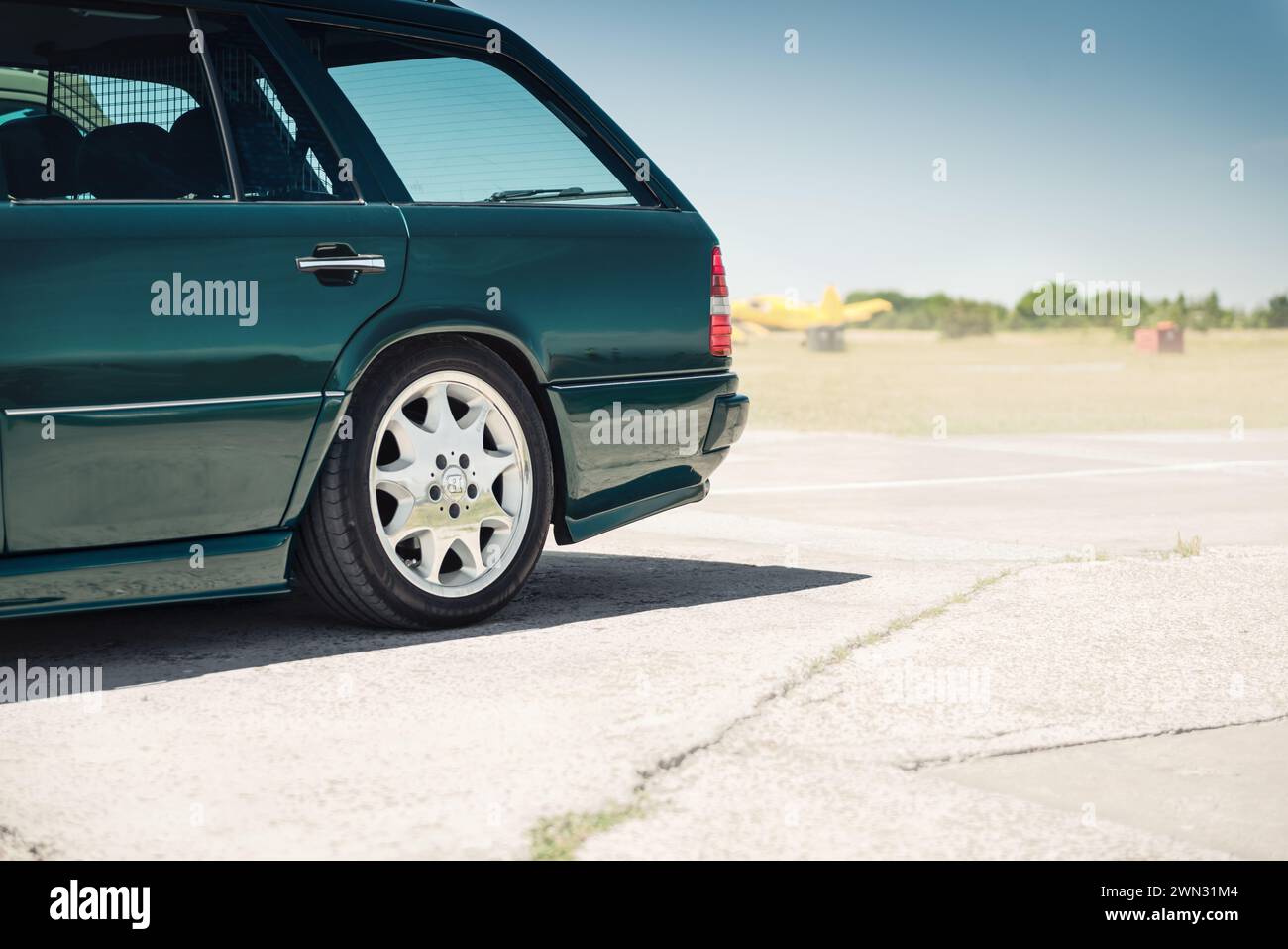 rear quarter of dark green Mercedes Benz wagon (W124 model). 1980s-1990s Mercedes with Brabus rims on a sunny day. Stock Photo