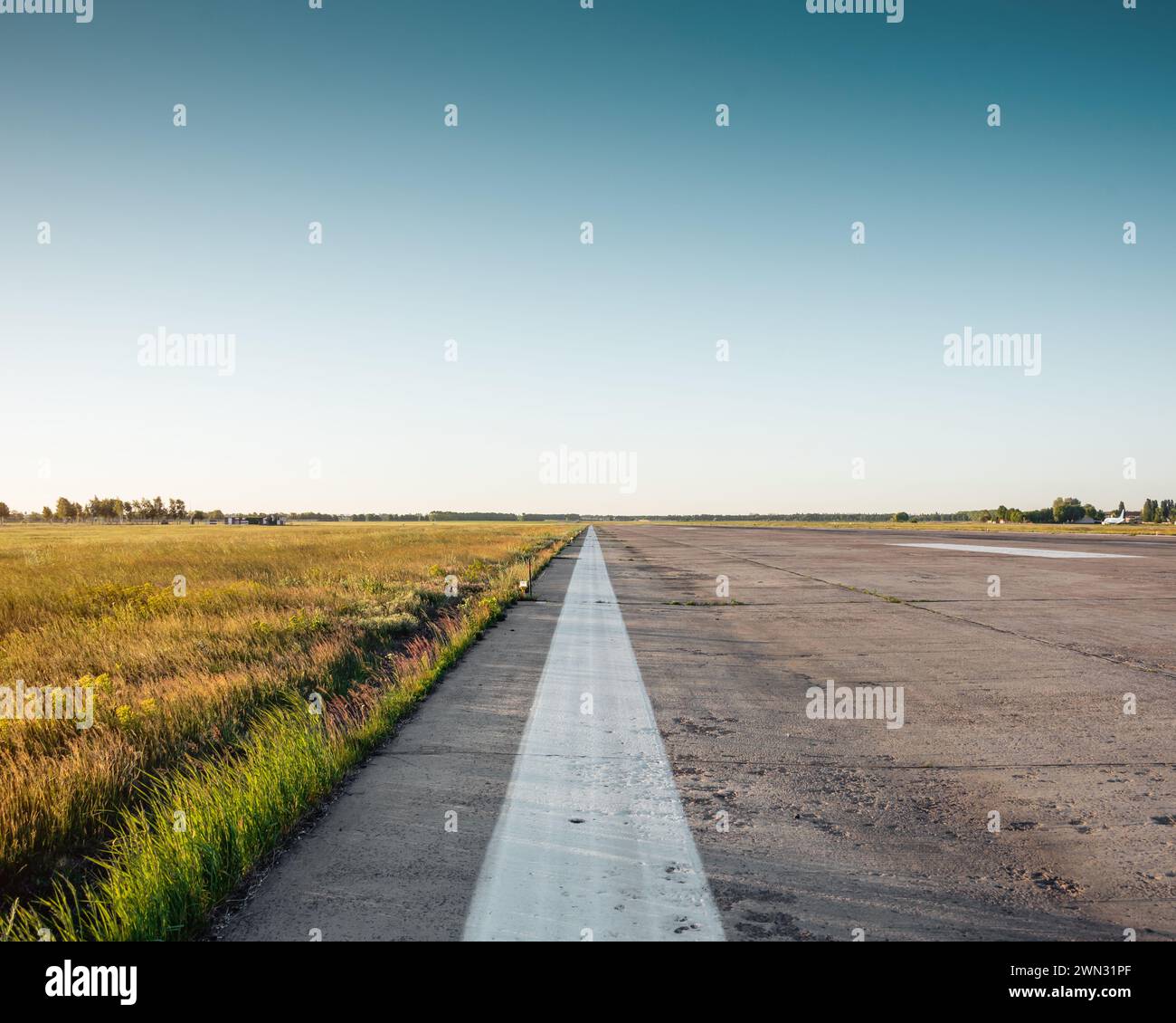 Endless white line. Road markings along the edge of airport runway. Minimalistic wide angle shot of empty airport runway at sunset - edge of runway. Stock Photo