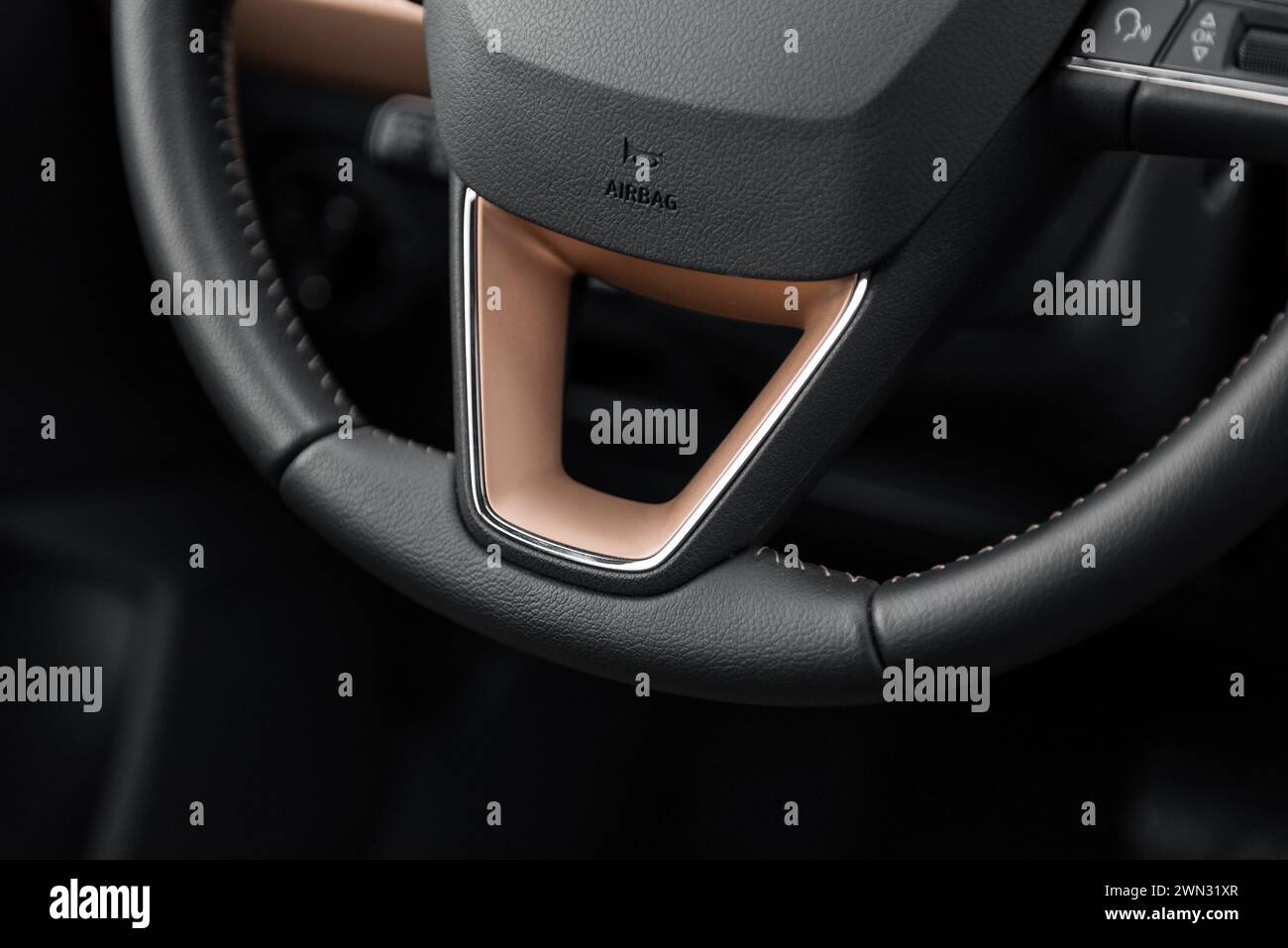 Bottom half of car steering wheel with copper elements. Leather steering wheel with beige stitching. Interior of modern compact car. Stock Photo