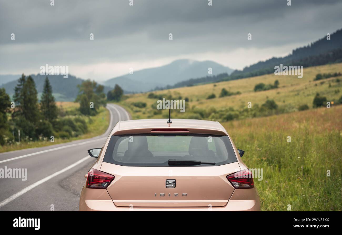 winding road in Carpathian mountains. Cloudy rainy weather in summer. Beige colored SEAT hatchback parked on the side of the mountain road. Stock Photo