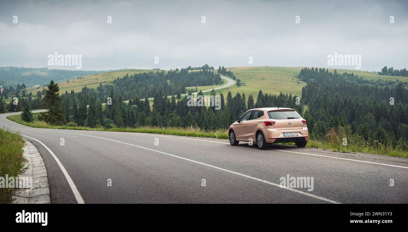 winding road in Carpathian mountains. Cloudy rainy weather in summer. Beige colored SEAT hatchback parked on the side of the mountain road. Stock Photo