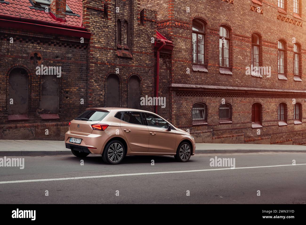 beige SEAT Ibiza in front of old brick building. Rear three quarter view of compact pale ivory spanish hatchback on downhill street in Lviv. Stock Photo