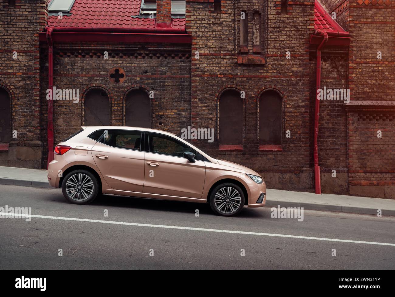 beige SEAT Ibiza in front of old brick building. Side profile view of compact pale ivory spanish hatchback on downhill street in Lviv. Stock Photo