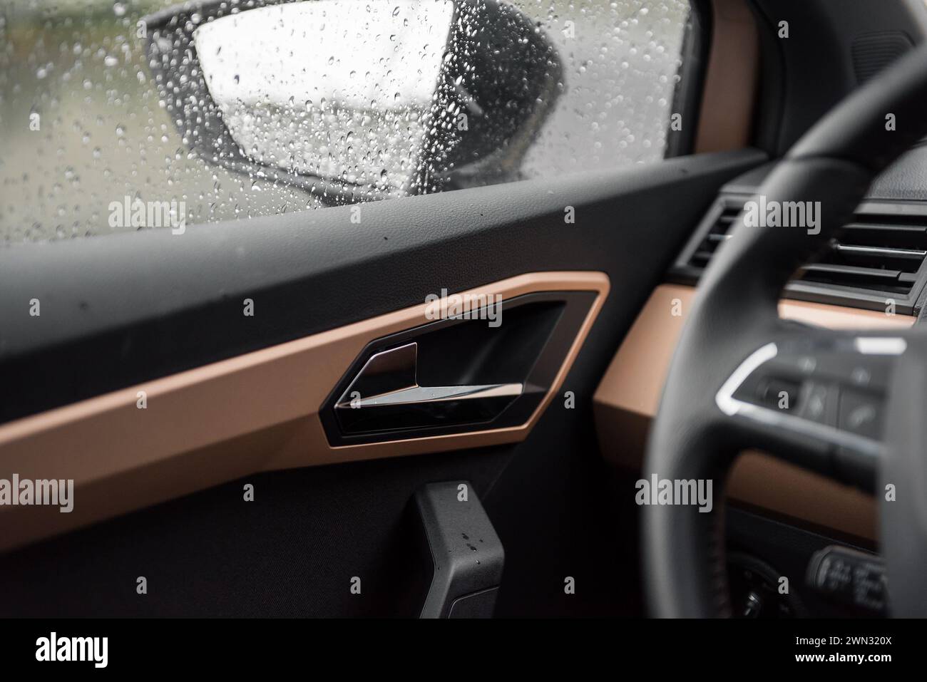 Driving in car in a rain. Cozy atmosphere and raindrops on widows. Car door handle and copper trim elements. Stock Photo