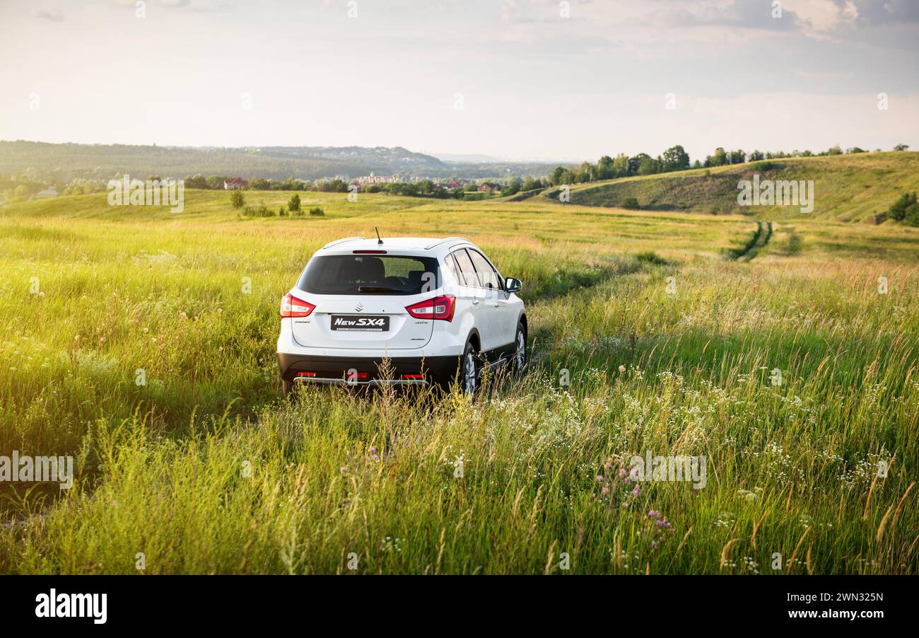 white Suzuki SX4 in a hilly countryside. Rear view of compact crossover in a green meadow - weekend away from the city Stock Photo
