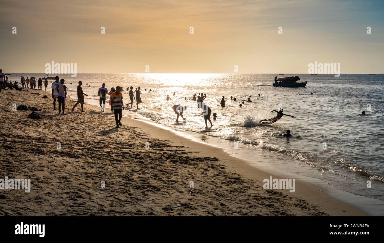 People in the sea and on the beach at sunset in Stone Town, Zanzibar, Tanzania Stock Photo