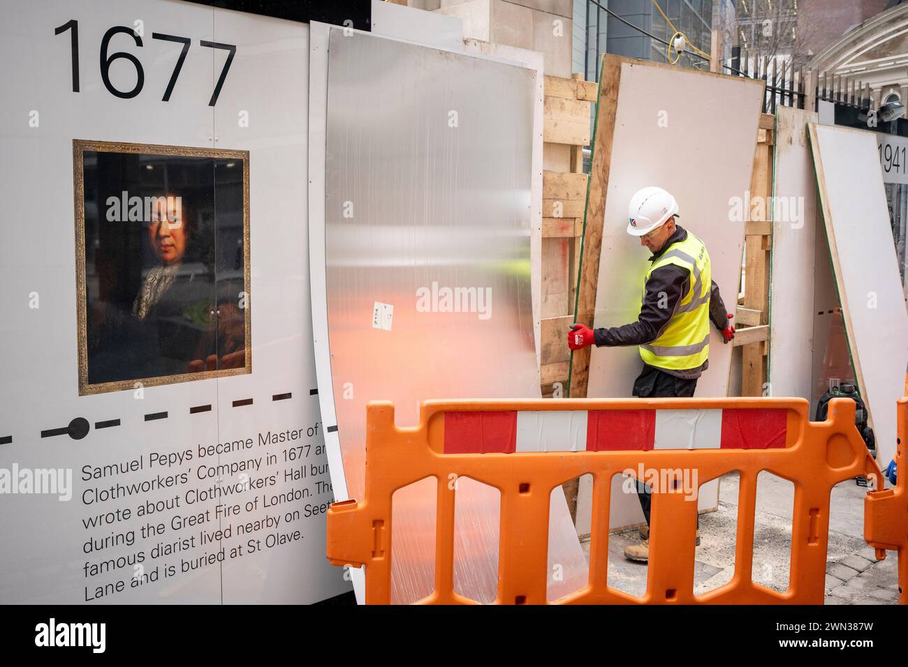 A contractor completes a protective hoarding that shows the face of Samuel Pepys and historical dates of the 12th century All Hallows church is surrounded by modern day construction activity in the City of London, the capital's financial district, on 28th February 2024, in London, England. All Hallows Staining (meaning constructed from stone, not wood) survived the Great Fire of London in 1666 and despite heavy damage, the Blitz in WW2. The site at 50 Fenchurch currently consists of the Grade I listed Tower of All Hallows Staining and the Grade II listed Lambe’s Chapel Crypt but construction i Stock Photo