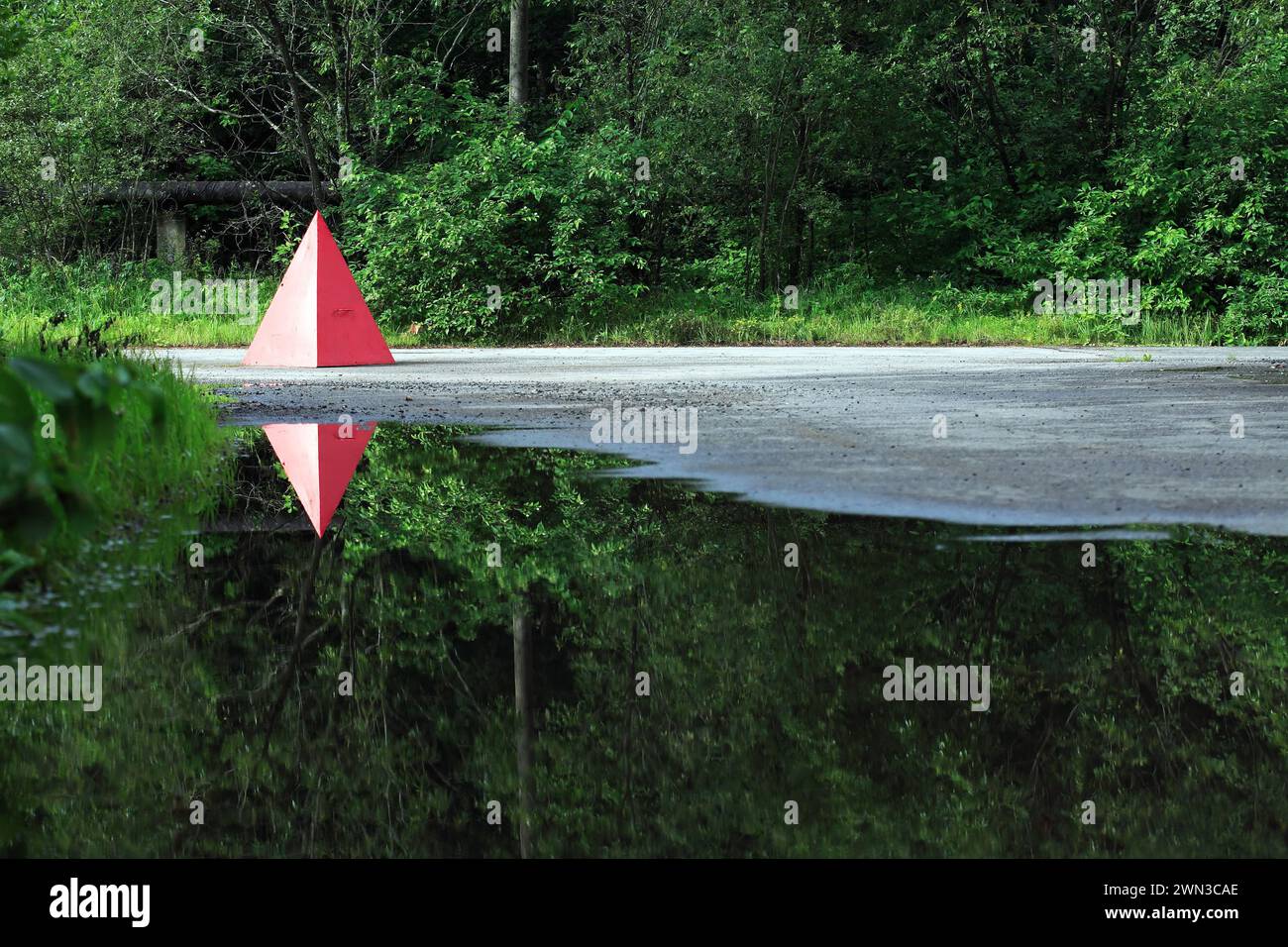 Red metal pyramid in forest with reflection in water Stock Photo