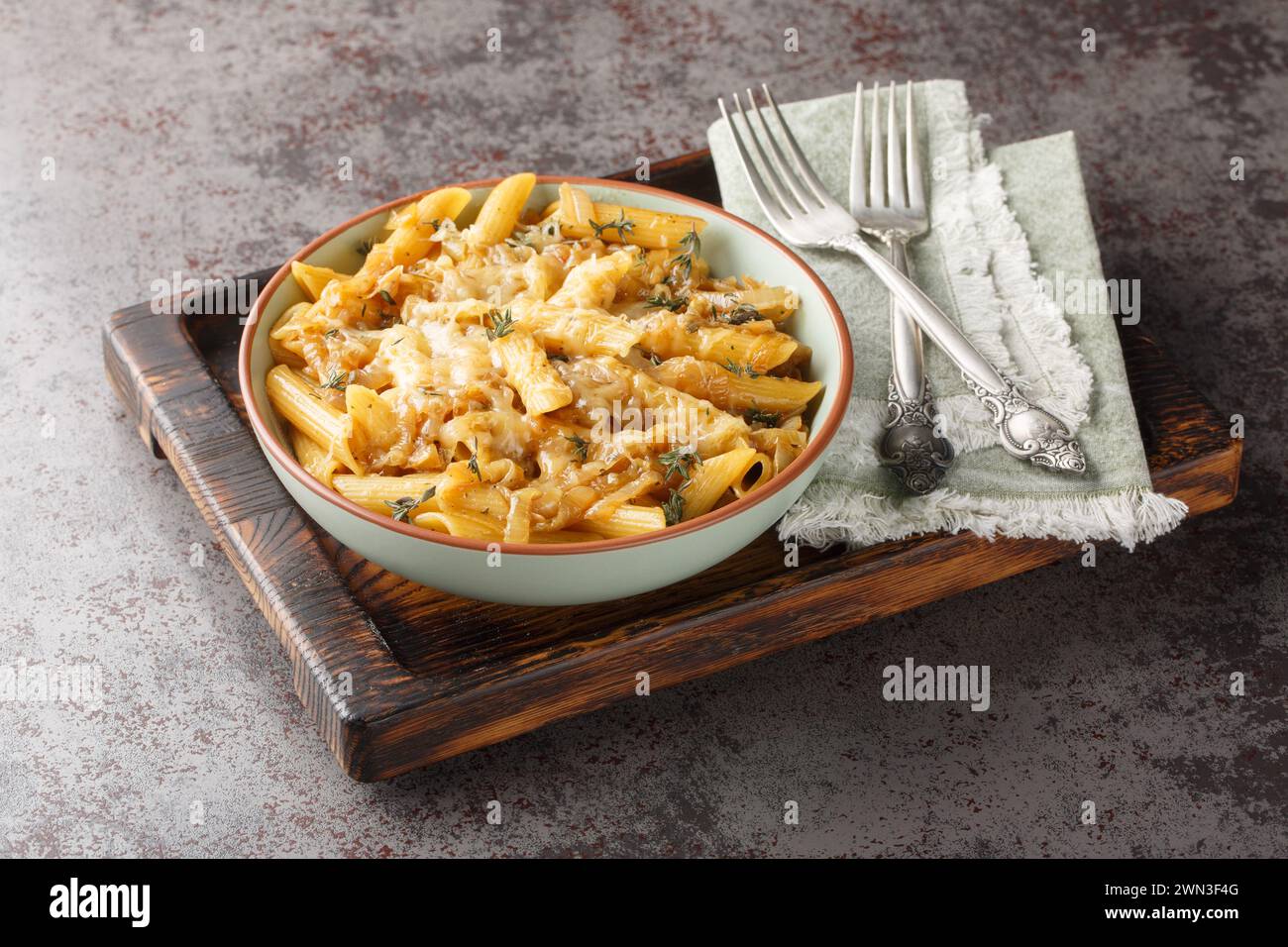 French Onion Style Creamy Pasta with caramelized onions, thyme, garlic and gruyere cheese close-up on a bowl on a wooden board. Horizontal Stock Photo