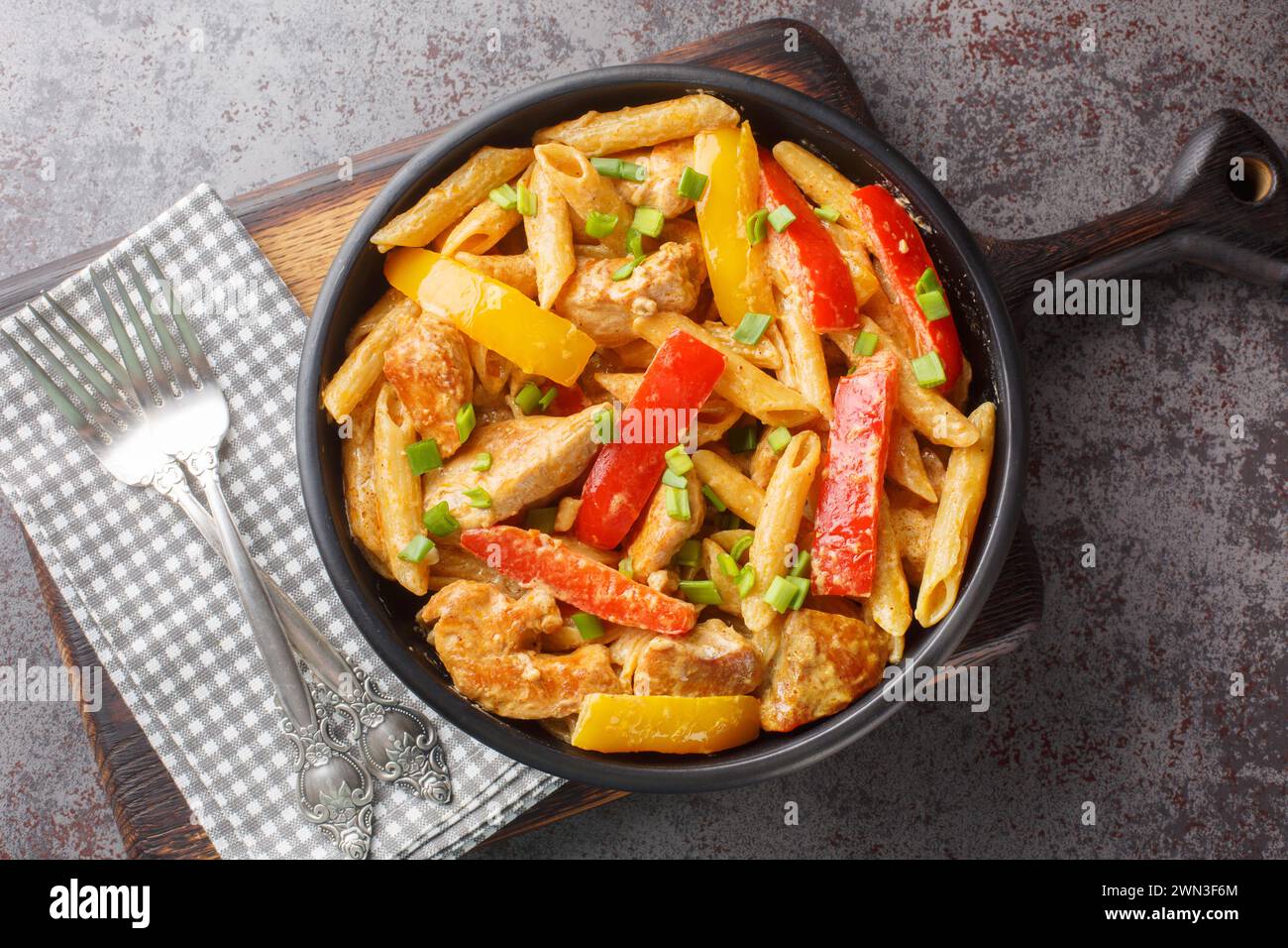 Rasta Pasta is a Penne cooked in rich creamy sauce with Jerk Chicken, sauteed onions, Sweet Peppers, garlic closeup on the bowl on the wooden board. H Stock Photo